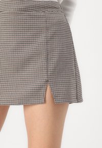 Fekete-fehér houndstooth mintás mini szoknya, enyhe hasítékkal a szegélyen és testhezálló derékrésszel. Sűrűn szőtt anyagból készült.