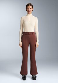 Kremast turtleneck s pletenim uzorkom s kratkim patentnim zatvaračem i dugim rukavima, uparen s burgundskim hlačama s flared krojem koje imaju obrubljene šavove i remen. Crna obuća.