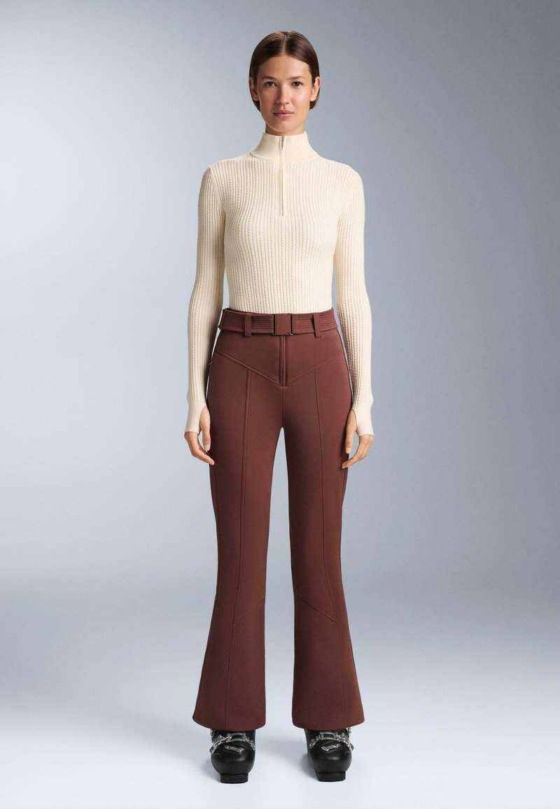 Kremast turtleneck s pletenim uzorkom s kratkim patentnim zatvaračem i dugim rukavima, uparen s burgundskim hlačama s flared krojem koje imaju obrubljene šavove i remen. Crna obuća.