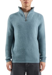 Jasnoniebieski wełniany sweter o teksturowanej powierzchni, wyposażony w krótkie stójkowe z zamkiem błyskawicznym oraz długie rękawy z prążkowanymi mankietami.