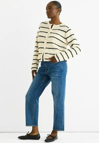 Cream striped cardigan with black lines, button closure, and textured fabric; paired with blue straight-leg jeans and black flats.