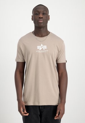 Beige cotton t-shirt featuring a white graphic logo, crew neck, short sleeves, and a small tag accent on the left side.