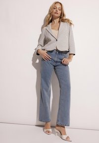 W paski czarno-biały krótki żakiet, niebieskie wysokie dżinsy i białe sandały na obcasie. Gładkie tekstury i luźny krój.