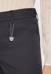 Čierne nohavice s hladkým povrchom, s pridaným strieborným reťazcom a ozdobou na páse. Mäkký vlnený sveter vo svetlo béžovej farbe.