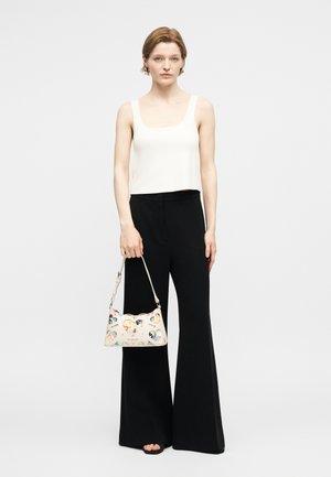 Γυναίκα που φορά λευκό αμάνικο τοπ και μαύρο παντελόνι φαρδιάς γραμμής, κρατώντας μια μικρή λευκή τσάντα χειρός με πολύχρωμες καρδιές σε σχέδιο κοπής.