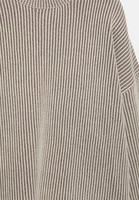 Pull tricoté à rayures verticales beiges et marron avec col montant côtelé et manches longues.