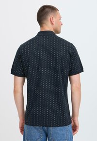 Polo noir à finition texturée, présentant un petit motif géométrique bleu, manches courtes et col en maille plate.