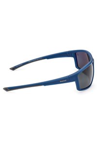 Gafas de sol polarizadas azules con un acabado mate, forma de lente angular y acentos negros en las patillas. Logo de Timberland cerca de la bisagra.
