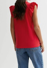 Haut rouge sans manches avec des accents volantés aux épaules, en tissu léger, associé à un jean denim bleu ample.