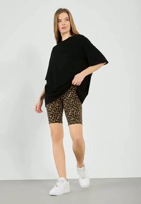 T-shirt nera oversize con maniche corte abbinata a pantaloni bike aderenti con stampa leopardata e sneakers bianche. Tessuto morbido, vestibilità rilassata.