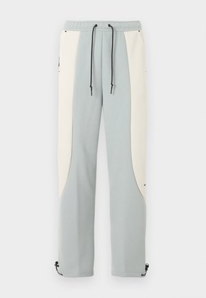 Vaaleansininen ja luonnonvalkoinen suoralahkeiset collegehousut mustilla säädettävillä vetoketjuilla ja nilkan soljilla.