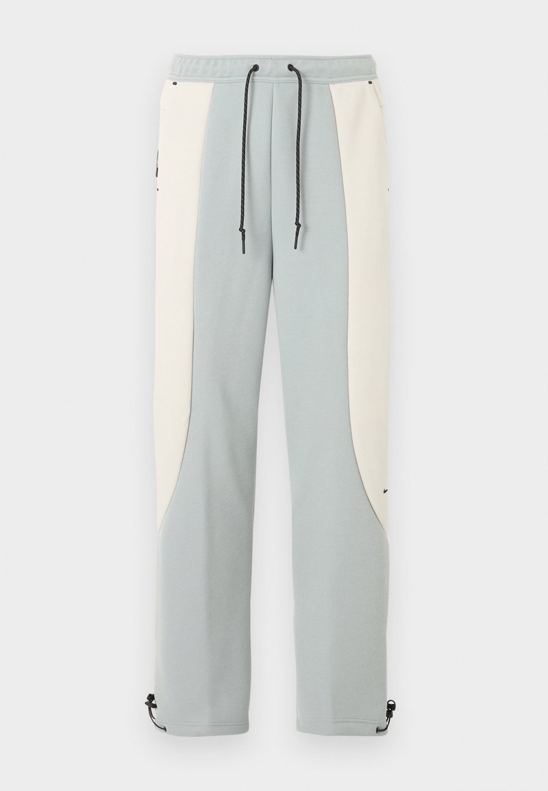 Pantalon de survêtement droit bleu clair et blanc cassé avec cordons de serrage noirs réglables et boutons-pression aux chevilles.