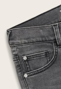 Šedé džíny z denimu s přiléhavým střihem, pěticí kapsami a kontrastním bílým prošíváním. Obsahují dva viditelné knoflíky na přední kapse.