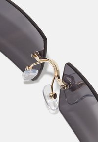 Sunglasses featuring gray tinted lenses with a gold metal bridge and clear nose pads. The arms are slightly curved and black.