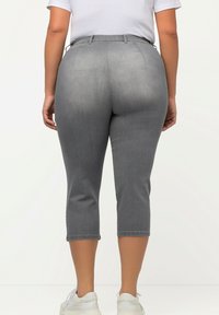Pantalons gris courts en denim, avec une taille haute et un design ajusté, dotés d'un ourlet net et de poches arrière. Portés avec des chaussures blanches.