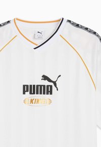 Hvid atletisk jersey med v-hals, sorte og guld detaljer, lodrette striber og et sort puma-logo med "PUMA KING" i fed tekst.