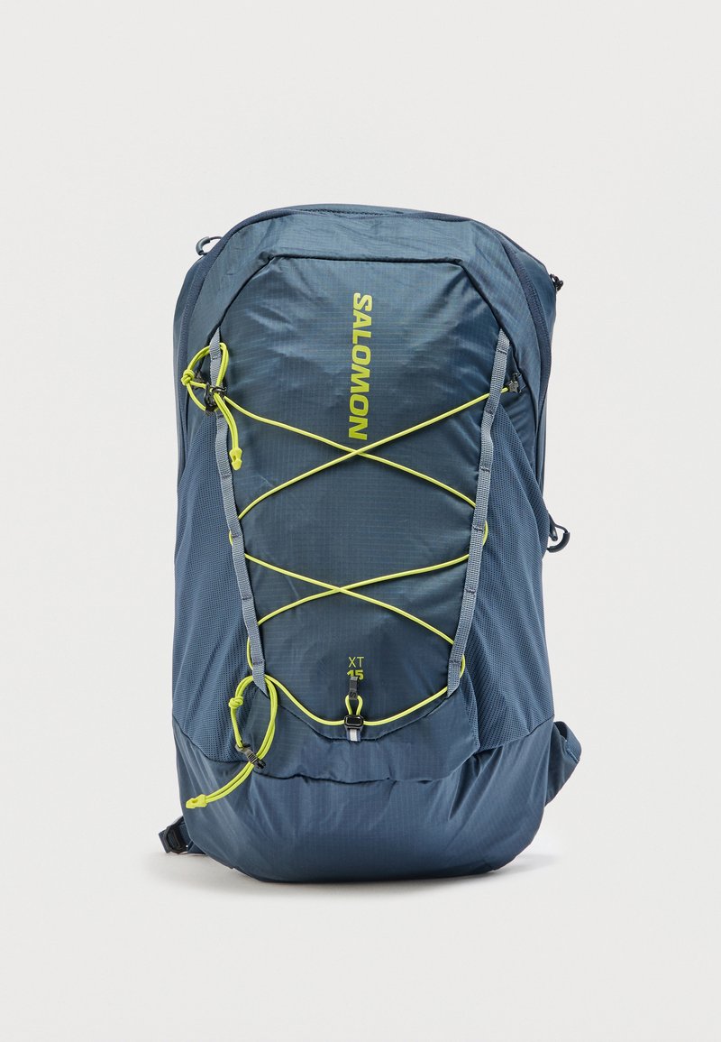 Μπλε σακίδιο πεζοπορίας Salomon XT 15 με κίτρινα ρυθμιζόμενα σχοινιά τύπου bungee και πλαινές θήκες από δίχτυ, μπροστινή όψη σε λευκό φόντο.