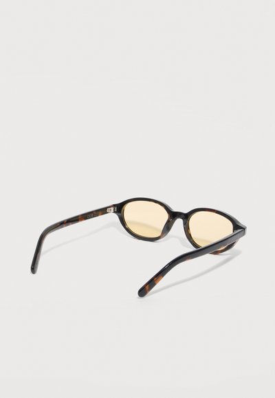 Tortoiseshell oval sunglasses with yellow tinted lenses resting open on white background.