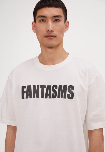 Hvit bomull T-skjorte med fet svart tekst "FANTASMS." Klassisk rund hals og løstsittende ermer. Glatt tekstur, minimalistisk design.