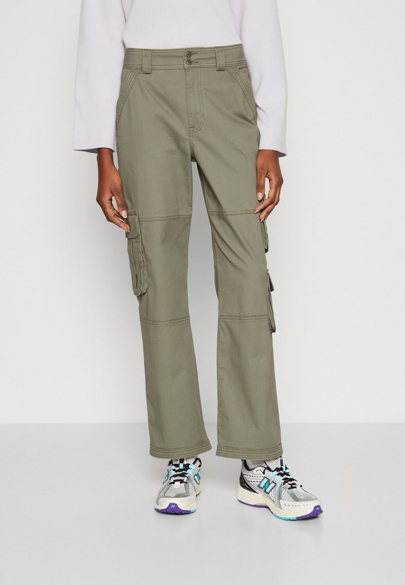Olive green cargo pants with a relaxed fit, featuring multiple pockets, contrasting stitching, and durable fabric. Paired with athletic sneakers.