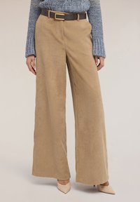 Spodnie szerokie z sztruksu w kolorze beżowym z pionowymi prążkami, zestawione z ciemnobrązowym paskiem z prostokątną złotą klamrą.