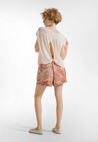 Lyserød kortærmet top med udskæring bagpå, parret med orange og hvide mønstrede shorts med tropisk bladdesign.