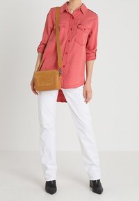 Koszula z długim rękawem, zapinana na guziki w kolorze koralowym, z dwiema przednimi kieszeniami, zestawiona z białymi spodniami i brązową torebką na ramię. Całość uzupełniają czarne botki za kostkę.