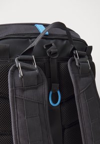 Sac à dos noir avec des bretelles en maille rembourrées et des accents bleus. Comprend des clips pour sécuriser les objets et un tissu texturé pour la durabilité.