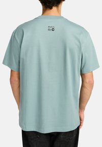 T-shirt in cotone azzurro chiaro con vestibilità rilassata. Presenta un collo rotondo e maniche corte. Sul retro è stampato il logo RVCA in nero.