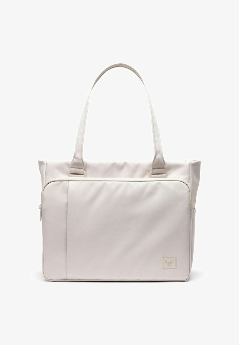 Sac fourre-tout beige clair avec deux poignées, une grande poche avant zippée, et une petite étiquette de marque en bas à droite.