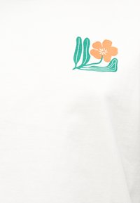 Πορτοκαλί λουλούδι με πέντε πέταλα και πράσινα καμπυλωτά φύλλα σε λευκό ύφασμα, τοποθετημένο κοντά στην περιοχή του άνω στήθους.