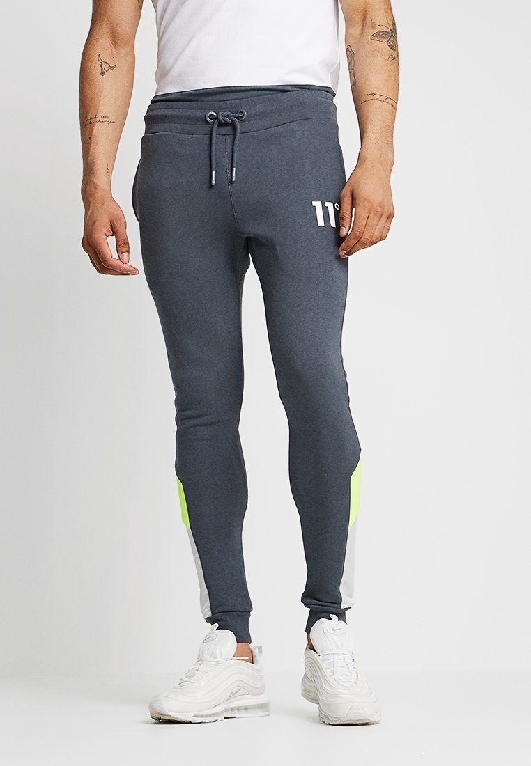 Grijze joggings met een neon groene accenten aan de zijkanten, voorzien van een elastische tailleband met koord en een wit logo op de linkerdij.