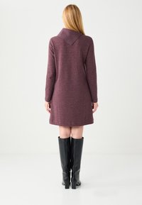 Robe en maille bordeaux avec un col large et des manches longues, associée à des bottes en cuir noires montant jusqu'au genou, présentée sur un fond blanc.