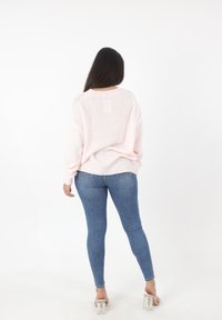 Hellrosa, gestrickter Pullover mit lockerem Sitz, gerippten Bündchen und Saum, kombiniert mit eng anliegenden blauen Jeans und klaren Sandalen mit Blockabsatz.