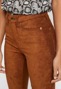 Pantaloni in simil pelle marroni con una texture liscia, design a vita alta, due tasche frontali e dettagli in metallo color oro.
