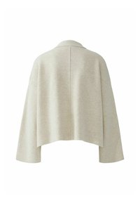Lichtbeige gebreide cardigan met een sjaalkraag, verlaagde schouders en een verkorte achterkant. De textuur is glad met een subtiele, zachte afwerking.