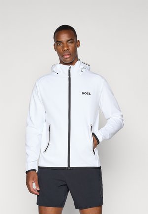 White zippered jacket with hood, black accents, side pockets, and "BOSS" logo. Worn over dark shorts. Smooth texture, sporty design.