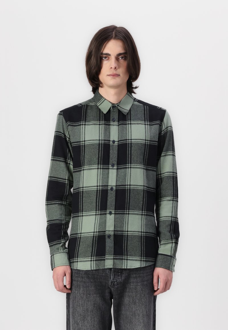 Camisa de cuadros en verde y negro, con cuello, mangas largas y botones oscuros. La tela parece de textura suave.