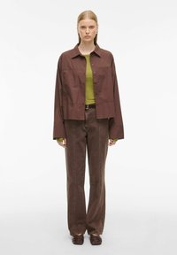 Bruine oversized shirtjack, groene aansluitende top, bruine high-waisted jeans en donkerbruine schoenen. Soepele stof, ontspannen silhouet.