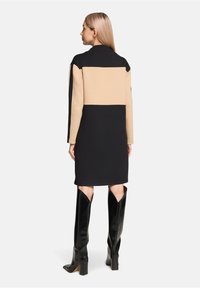 Płaszcz w czarno-beżowe bloki kolorystyczne o długości do kolan. Posiada długie rękawy i prosty krój, zestawiony z czarnymi kozakami sięgającymi do kolan.