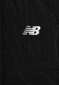 Black fabric with white embroidered New Balance logo featuring stylized "NB" letters and horizontal speed lines.
