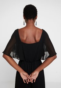 Black dress with sheer flutter sleeves, scooped back, and fitted waist. Smooth, flowing fabric with an elegant silhouette.
