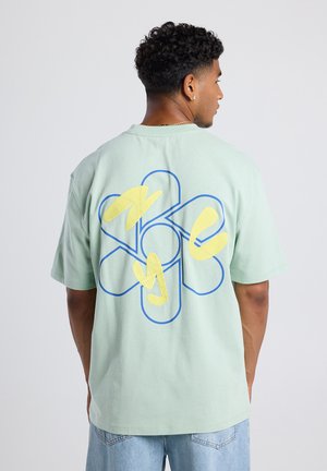 Lichtgroene katoenen t-shirt met een groot bloemenontwerp in blauwe omranding en gele accenten op de achterkant, casual fit en korte mouwen.