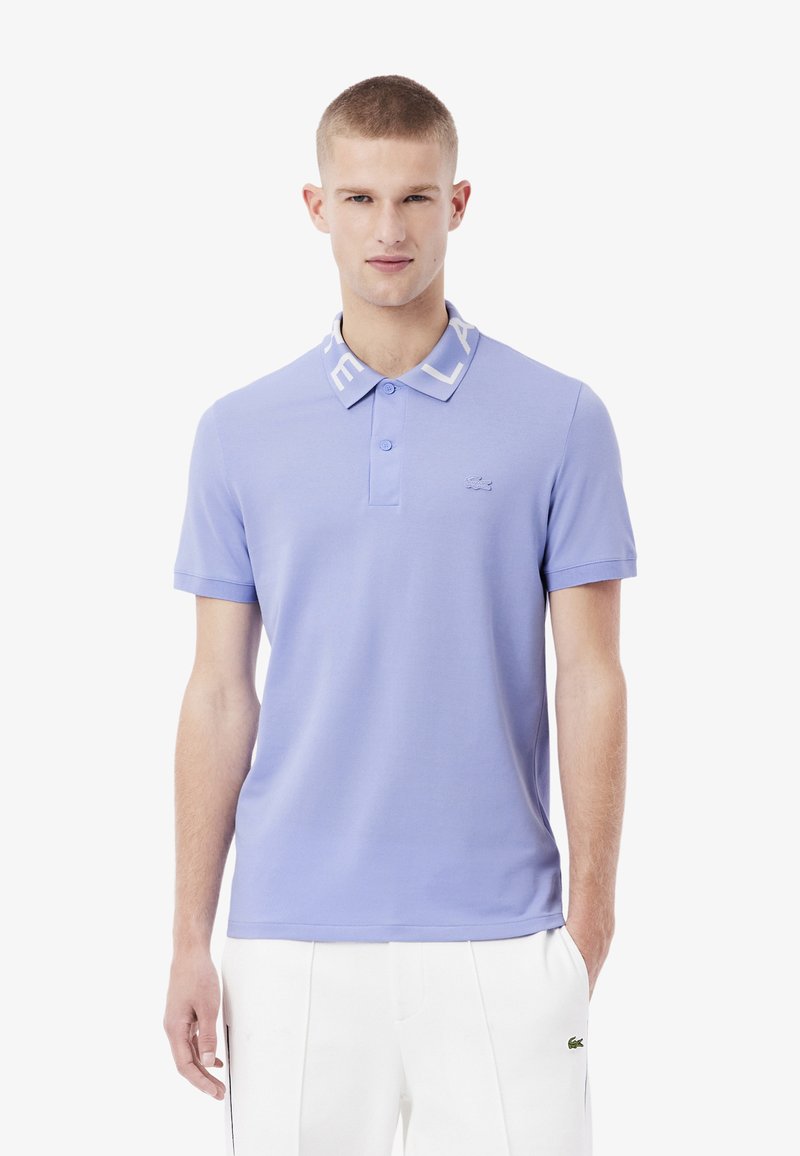 Lichtpaarse polohemd gemaakt van zachte stof, met een witte kraag met tekst, een placket met drie knopen en een klein logo op de borst.