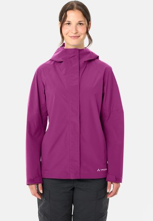 Frau trägt eine violette wasserdichte Jacke mit Kapuze, steht vor einem einfarbigen hellen Hintergrund und lächelt leicht.