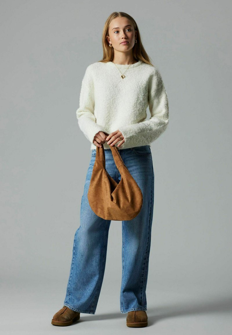 Weißer strukturierter Pullover, blaue weite Jeans und braune Tasche aus weichem Stoff. Accessoires umfassen eine goldene Kette und Ohrringe.