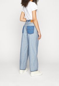 Jasnoniebieskie, szerokie dżinsy z kontrastowymi tylniymi kieszeniami. Pasa zdobi brązowa skórzana naszywka. Stylizowane z białą koszulką i sneakersami.