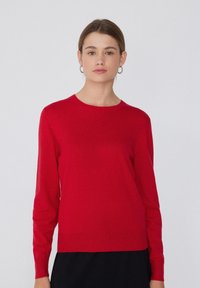 Pull rouge à manches longues en tissu doux, avec un col ras du cou et des poignets côtelés, présentant une coupe droite et un design minimaliste.