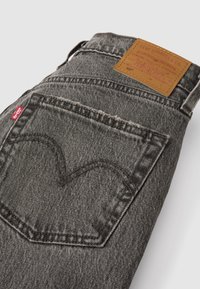 Donkergrijze denim jeans met een leren patch met het merklogo en stikseldetails. Het achterzakje heeft een iconisch rood label.
