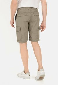 Khaki cargo shorts met meerdere zakken, gemaakt van lichtgewicht stof, met een ontspannen pasvorm en afgewerkte zoom. Slanke witte sneakers zichtbaar.